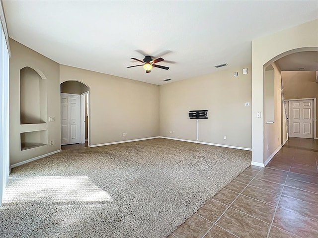 empty room featuring visible vents, dark tile patterned floors, dark carpet, baseboards, and ceiling fan