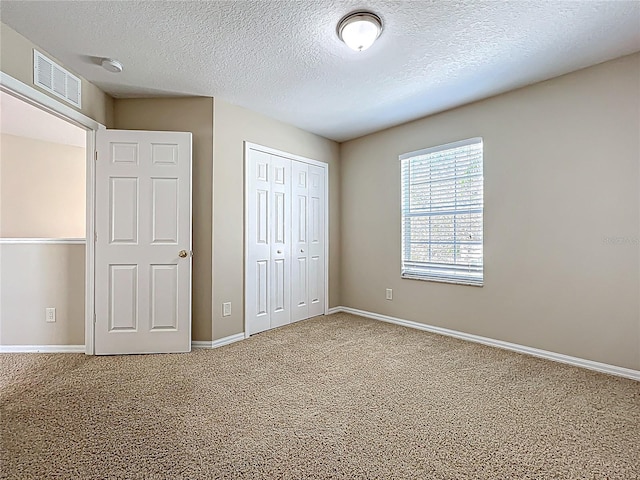 unfurnished bedroom with visible vents, a textured ceiling, a closet, carpet, and baseboards