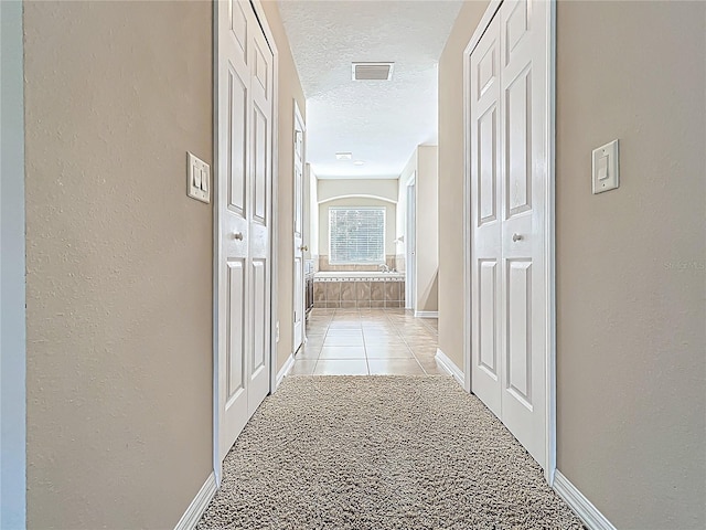 hallway featuring visible vents, a textured ceiling, baseboards, and a textured wall