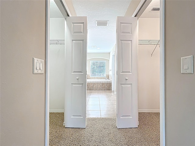 hallway with visible vents, baseboards, a textured ceiling, and light carpet