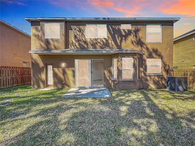 back of house featuring stucco siding, a lawn, central AC, and fence