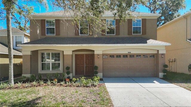 traditional-style house with stucco siding, an attached garage, roof with shingles, and driveway