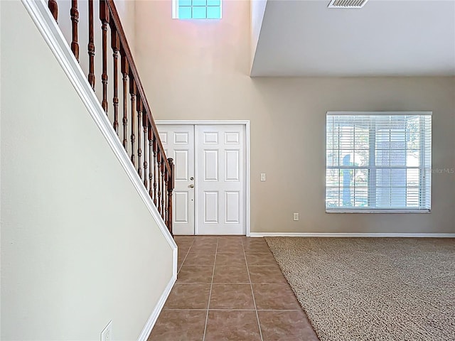 tiled foyer entrance featuring stairs, a high ceiling, visible vents, and baseboards