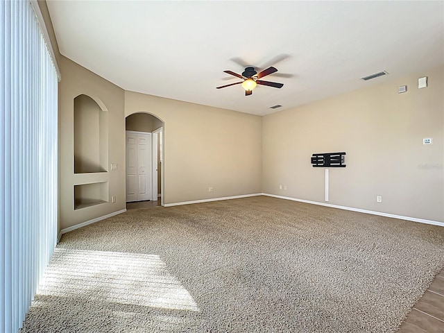 carpeted spare room featuring baseboards, visible vents, arched walkways, and ceiling fan