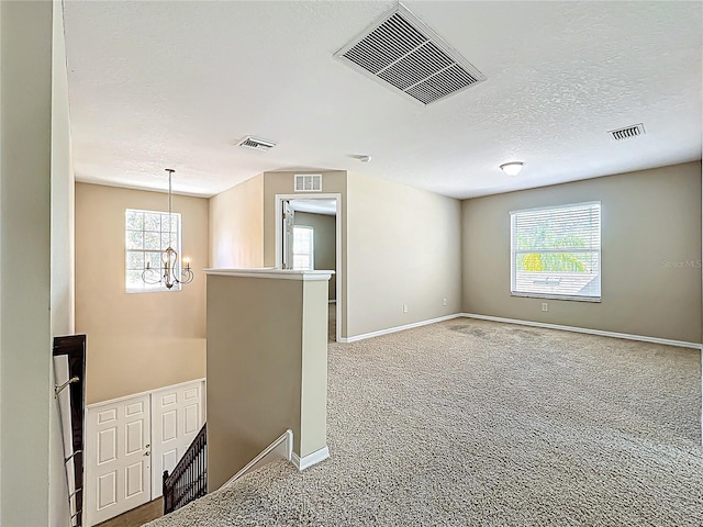 carpeted empty room with an inviting chandelier, visible vents, and a textured ceiling