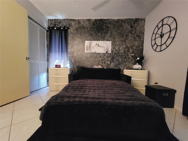 tiled bedroom with a closet, a textured ceiling, and an accent wall