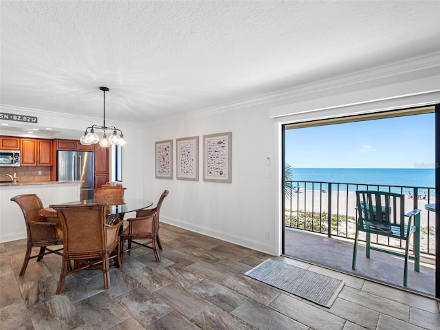 dining room featuring baseboards, a water view, ornamental molding, a notable chandelier, and a textured ceiling