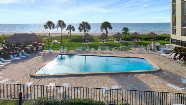 community pool featuring a patio, a lawn, a water view, and fence