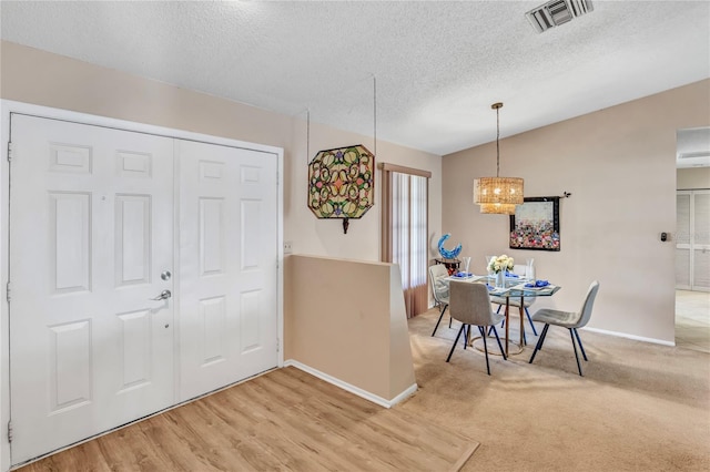 dining area featuring visible vents, baseboards, vaulted ceiling, light carpet, and a textured ceiling