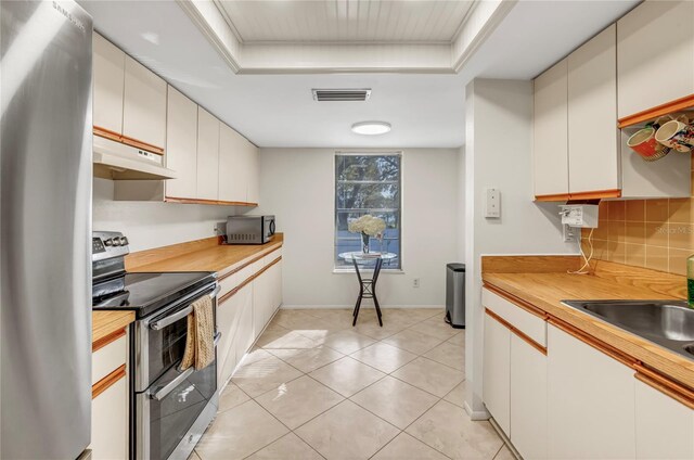 kitchen featuring visible vents, under cabinet range hood, a tray ceiling, decorative backsplash, and stainless steel appliances