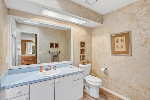 bathroom with toilet, wood finished floors, wallpapered walls, baseboards, and vanity