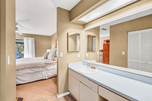 ensuite bathroom with baseboards, ceiling fan, vanity, a textured ceiling, and ensuite bath