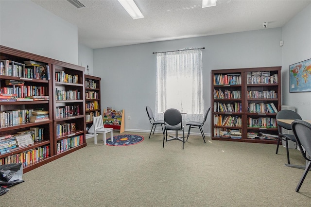 living area with bookshelves, a textured ceiling, baseboards, and carpet floors