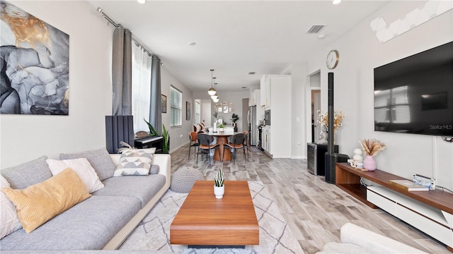 living room with baseboards, visible vents, light wood finished floors, and a baseboard radiator