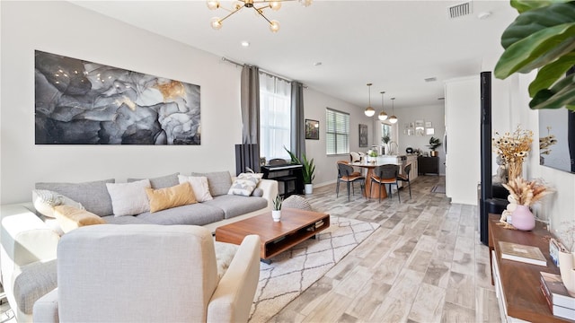 living room featuring light wood-type flooring, visible vents, baseboards, and a chandelier