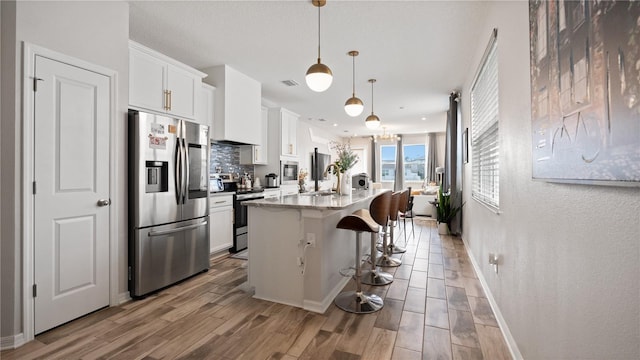 kitchen featuring a breakfast bar area, wood finished floors, stainless steel appliances, white cabinets, and backsplash