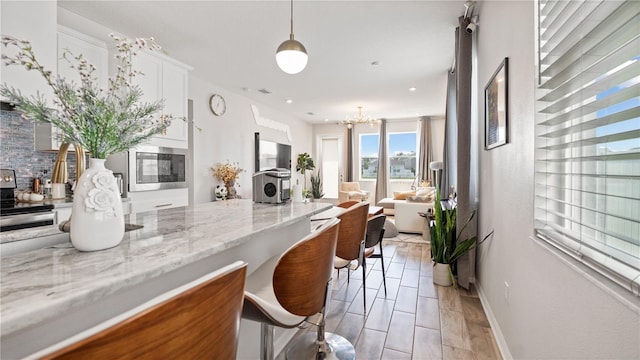 kitchen featuring open floor plan, stainless steel appliances, an inviting chandelier, white cabinets, and light stone countertops