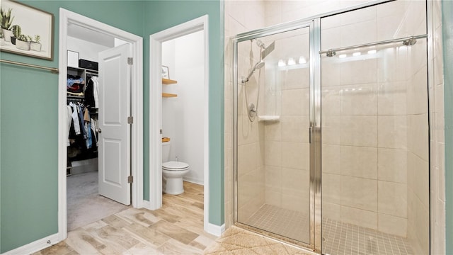 bathroom featuring a spacious closet, toilet, baseboards, and a stall shower