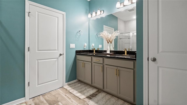 bathroom featuring a shower stall, wood finished floors, double vanity, and a sink