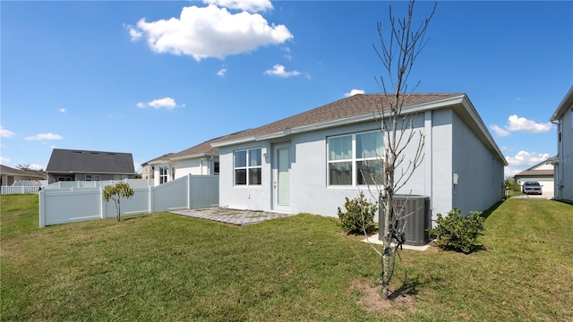 rear view of house featuring stucco siding, a lawn, central AC, and fence