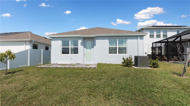 back of property with fence, a yard, stucco siding, a lanai, and central air condition unit