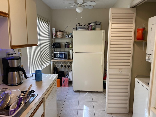 kitchen featuring stainless steel microwave, stacked washer and clothes dryer, freestanding refrigerator, light tile patterned flooring, and a ceiling fan