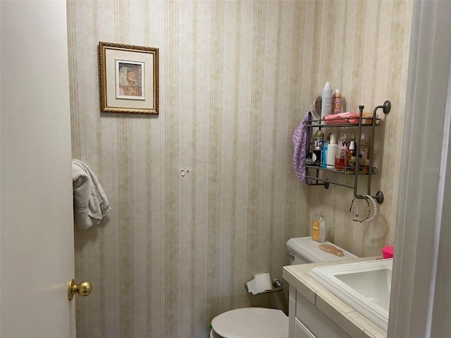 bathroom with toilet, vanity, and wallpapered walls