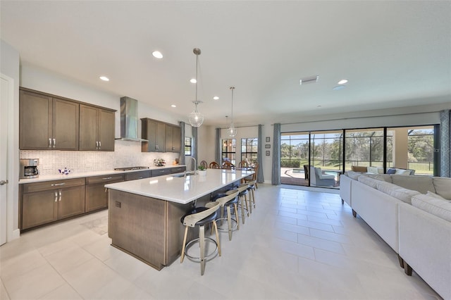 kitchen featuring backsplash, open floor plan, a breakfast bar, wall chimney exhaust hood, and a sink