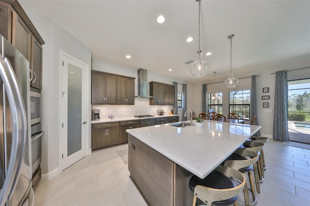 kitchen featuring a sink, tasteful backsplash, stainless steel appliances, wall chimney exhaust hood, and a large island with sink