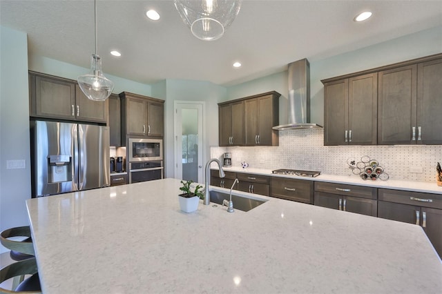 kitchen with a sink, stainless steel appliances, wall chimney exhaust hood, and decorative backsplash