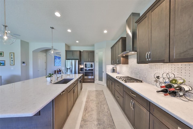 kitchen featuring a sink, tasteful backsplash, arched walkways, appliances with stainless steel finishes, and wall chimney range hood