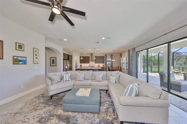 living area featuring light tile patterned floors, recessed lighting, arched walkways, and baseboards