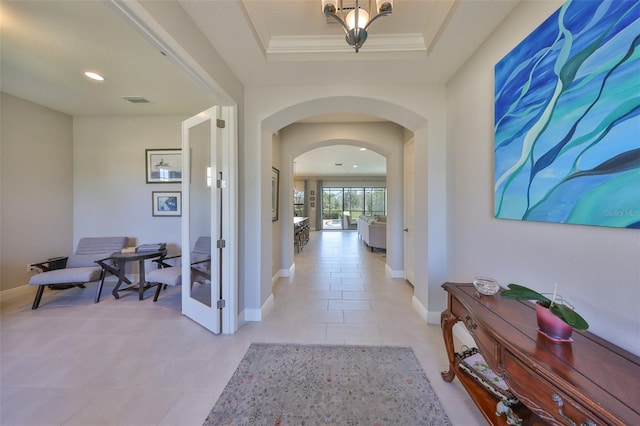 corridor with a raised ceiling, baseboards, and arched walkways