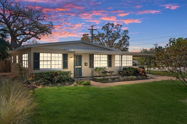 view of front facade featuring a yard, a carport, and concrete block siding