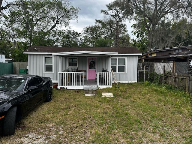 view of front of house with covered porch, board and batten siding, a front lawn, and fence