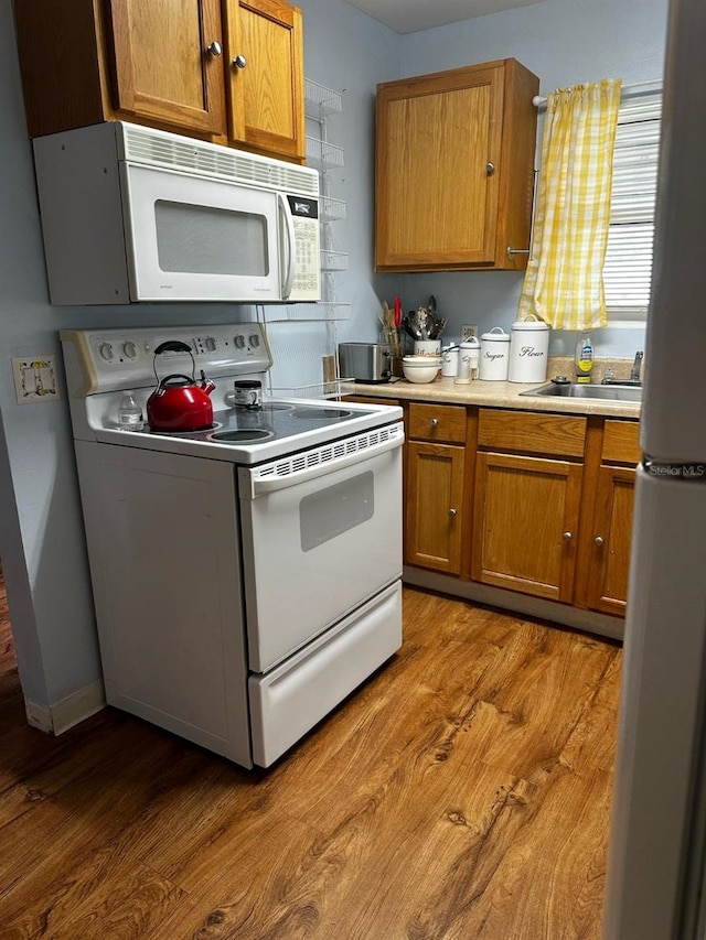 kitchen featuring white appliances, light wood-style flooring, brown cabinets, and a sink