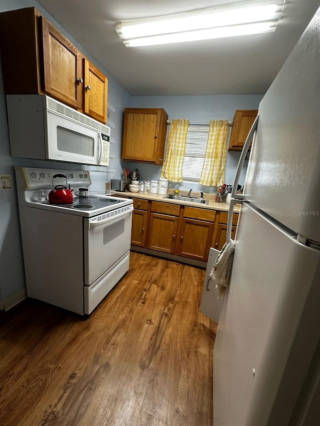 kitchen featuring white appliances, brown cabinetry, dark wood-style flooring, and a sink