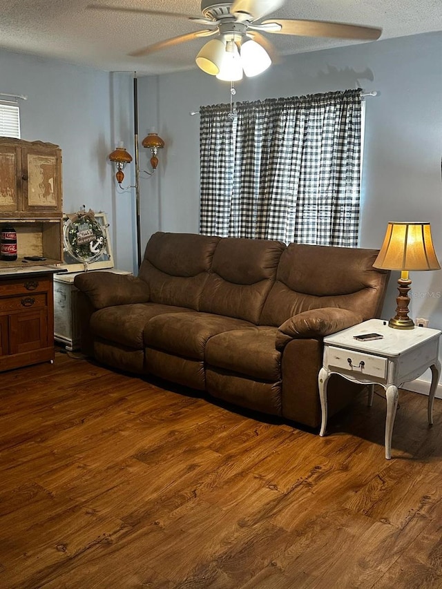 living room featuring dark wood-type flooring, a ceiling fan, and a textured ceiling