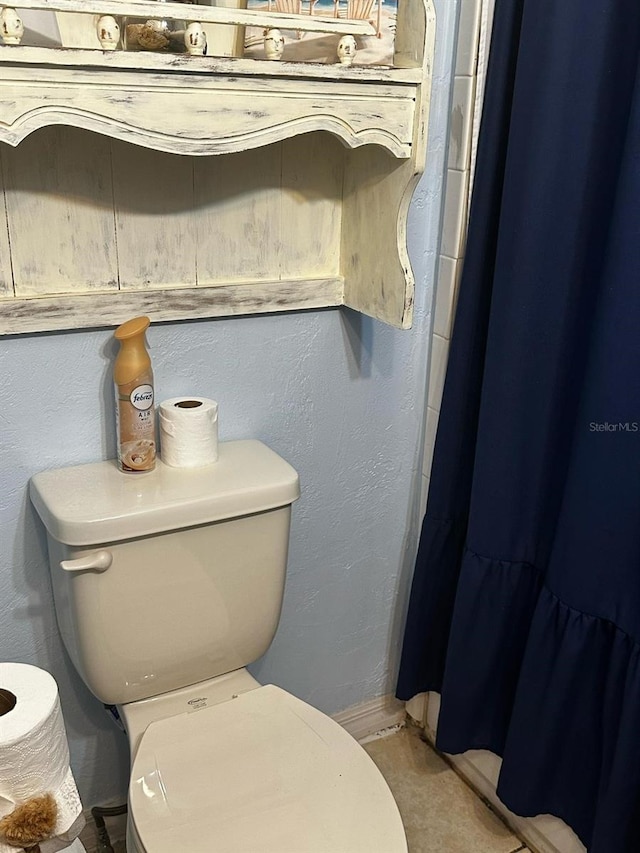 full bathroom with a shower with shower curtain, toilet, and a textured wall