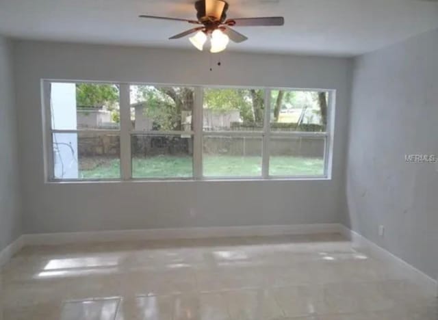 spare room featuring a wealth of natural light, a ceiling fan, and baseboards