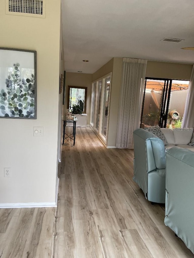 hall featuring baseboards, visible vents, and light wood finished floors