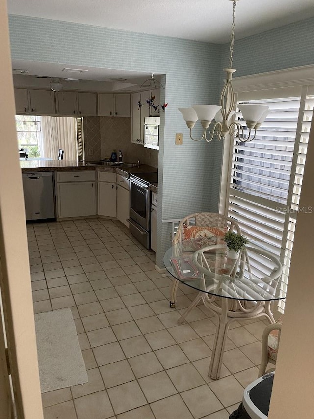 kitchen with wallpapered walls, a chandelier, light tile patterned floors, appliances with stainless steel finishes, and white cabinets