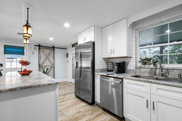 kitchen with a barn door, light wood-style flooring, appliances with stainless steel finishes, white cabinetry, and a sink