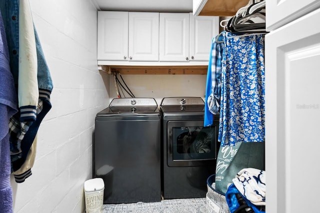 clothes washing area featuring concrete block wall, cabinet space, and independent washer and dryer