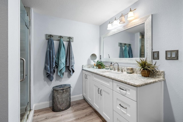 bathroom featuring vanity, wood finished floors, baseboards, a shower stall, and a textured ceiling