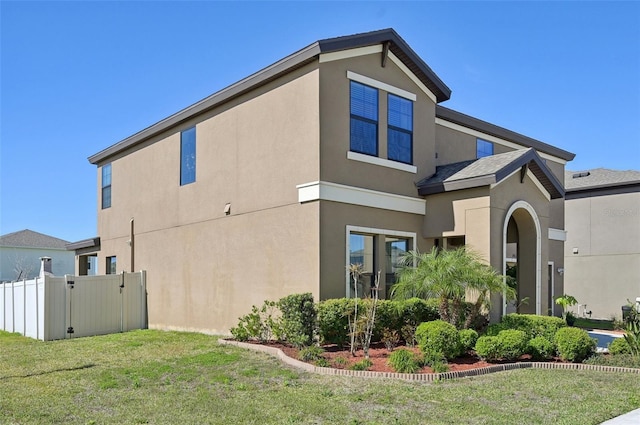 view of side of home with stucco siding, a lawn, and fence