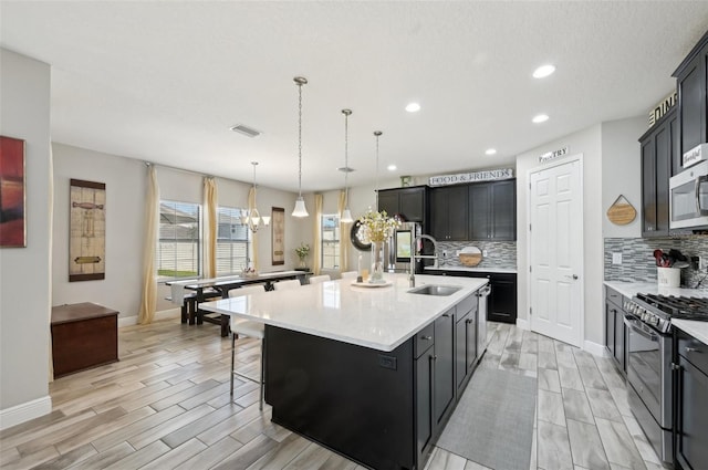 kitchen with visible vents, backsplash, a center island with sink, appliances with stainless steel finishes, and a sink