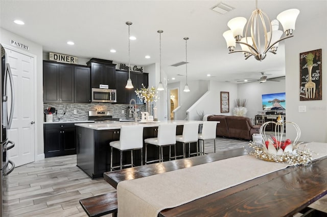 kitchen featuring visible vents, a kitchen island with sink, backsplash, open floor plan, and appliances with stainless steel finishes