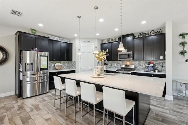 kitchen featuring visible vents, dark cabinets, a breakfast bar, stainless steel appliances, and a kitchen island with sink