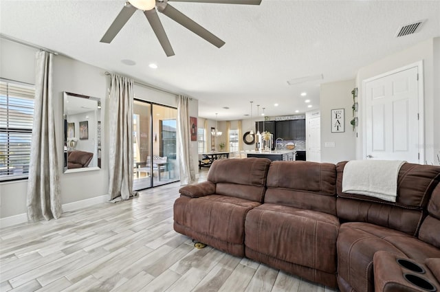 living room featuring ceiling fan, visible vents, a textured ceiling, and light wood-style flooring